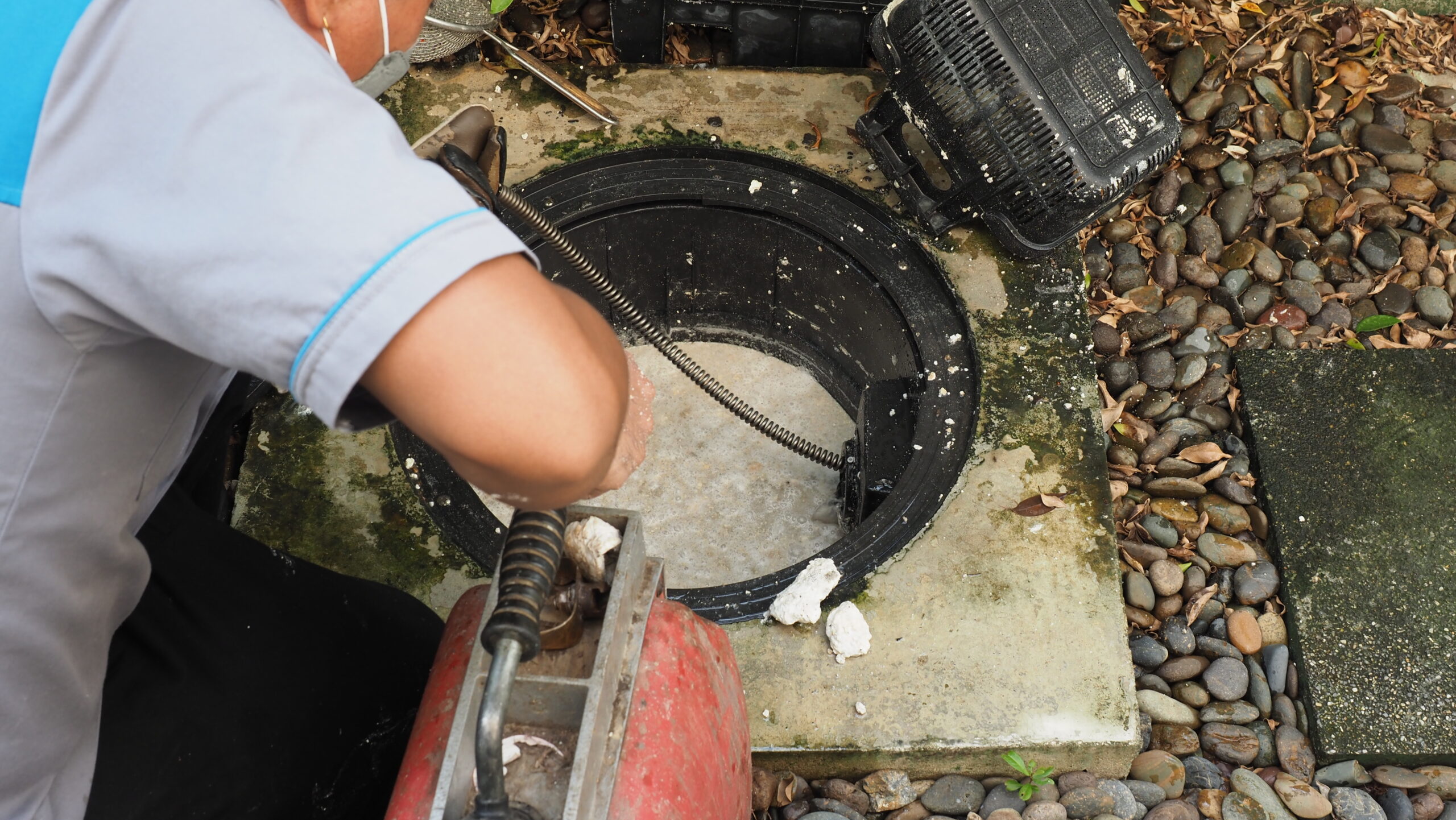 Drain cleaning. Plumber repairing clogged grease trap with auger machine. Maintenance the sewage system and grease trap by professional plumber. Using auger snake to fix and unclog a drain.